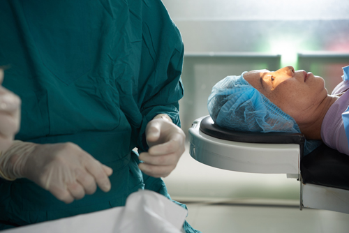 Grauer Star OP (Katarakt OP): Arzt steht am Kopfende eines OP-Tisches mit Patientin